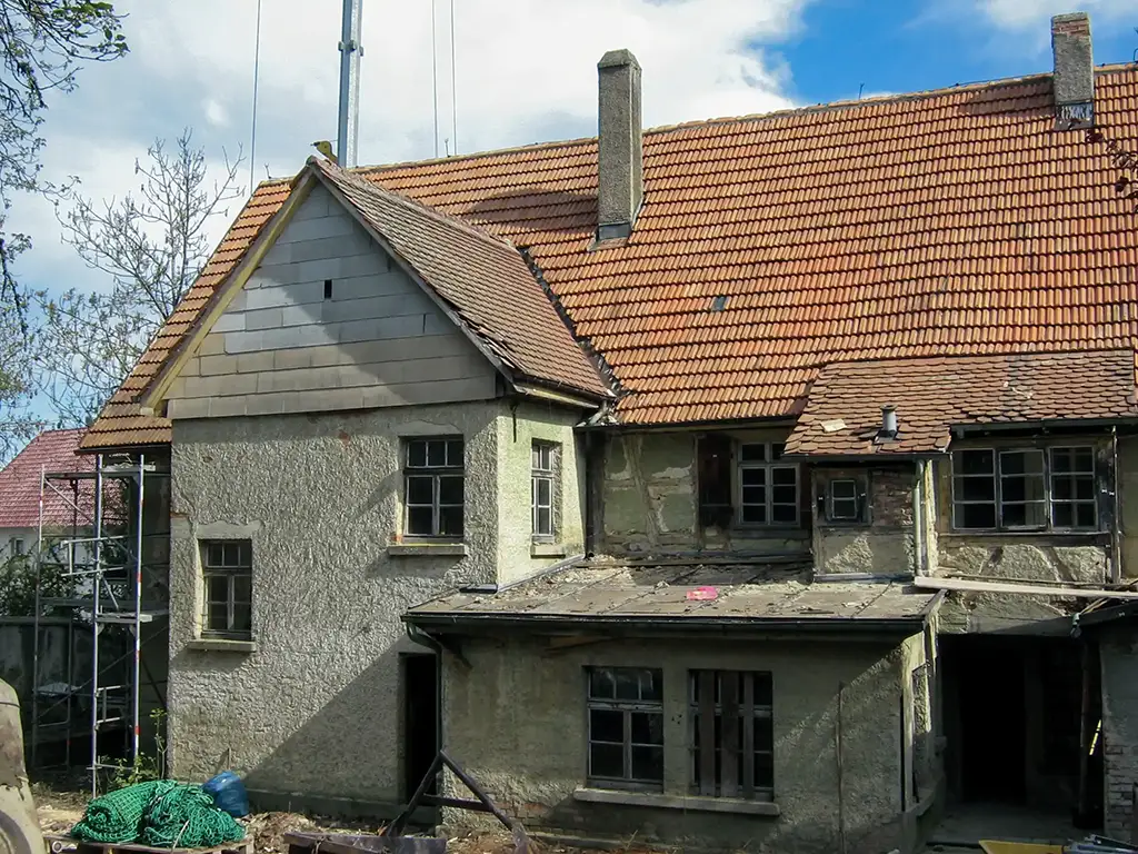 Rückseite des renovierungsbedürftigen Kaufhauses Pfeiffer, mit verwittertem Mauerwerk und Ziegeldach. Das Haus ist umgeben von Gerüsten und Baumaterialien.