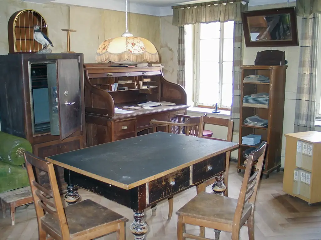 Historischer Büroraum mit einem dunklen Holztisch, Stühlen und einem antiken Schreibtisch.