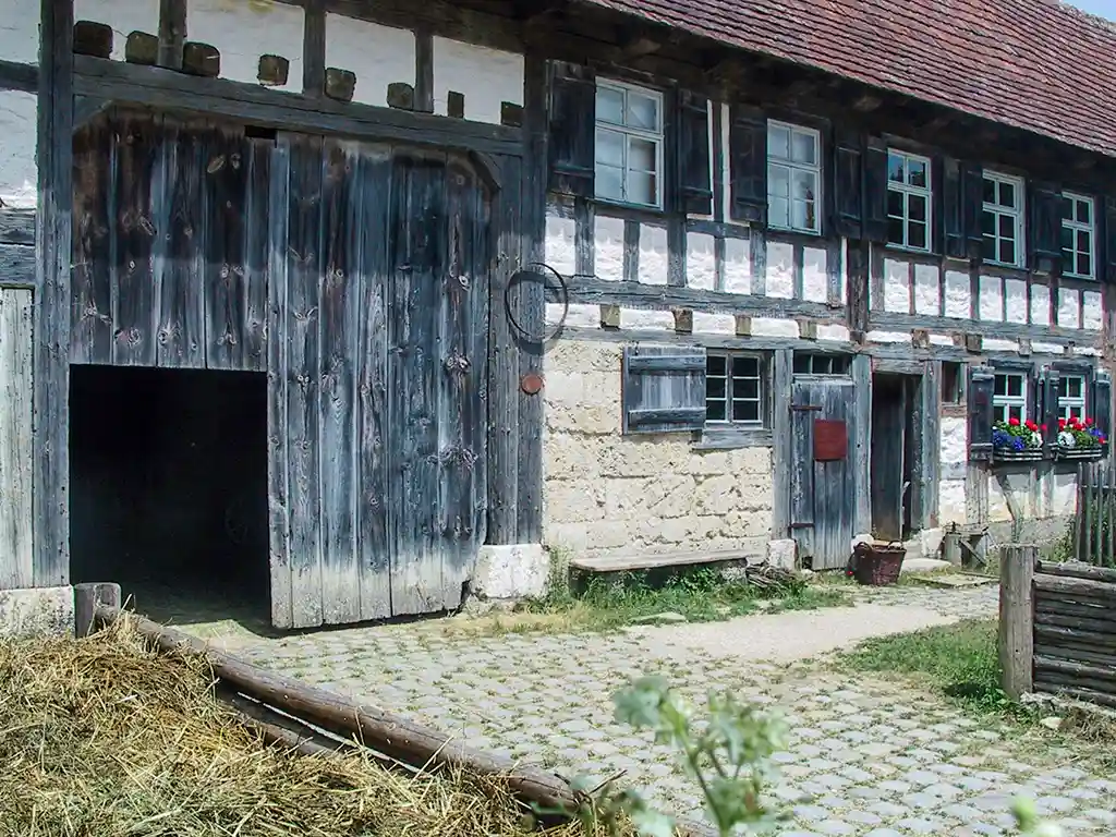 Fachwerkhaus von außen. Eine Scheune mit großen Holztoren und einem Stallbereich mit Stroh.