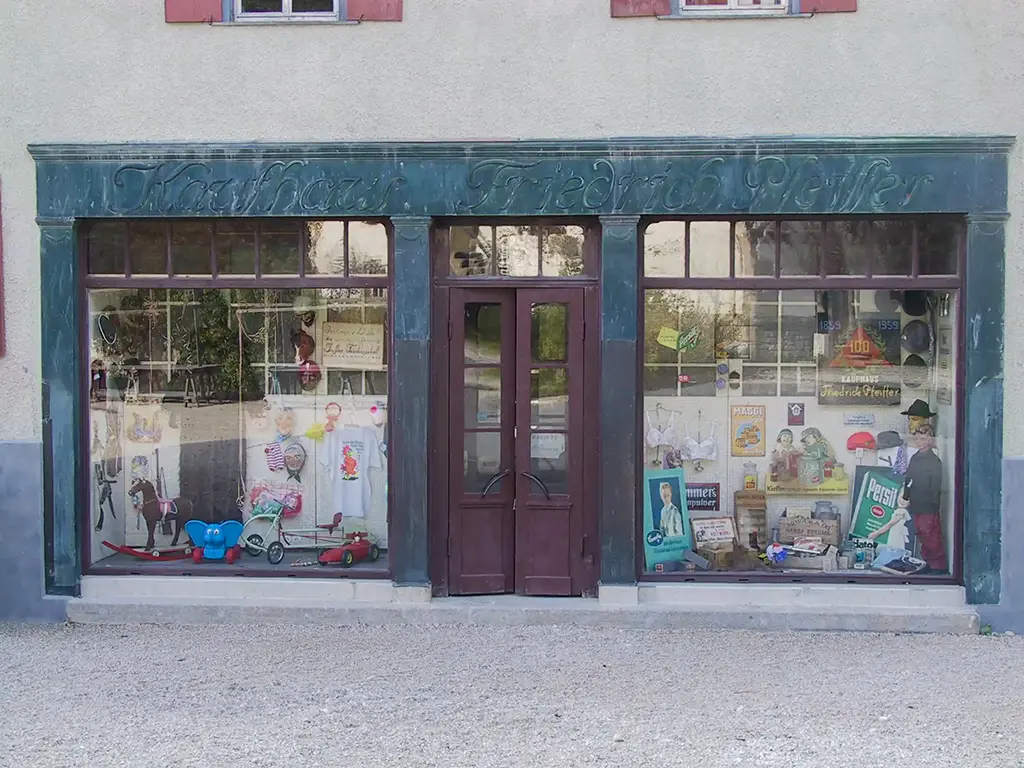 Historische Ladenfassade mit zwei großen, bunt dekorierten Schaufenstern und Doppeltür.