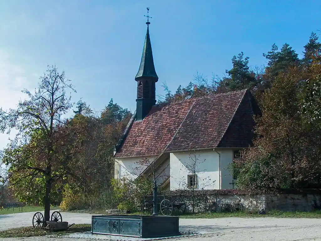 Außenansicht der Dorfkirche Tischardt mit spitzem Kirchturm und Fachwerkfassade, umgeben von Bäumen.