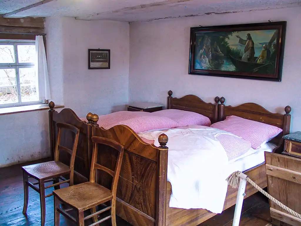 Ein traditionelles Schlafzimmer mit einem Doppelbett, weiß-rot karierter Bettwäsche und Holzmöbeln. An der Wand ein Gemälde.