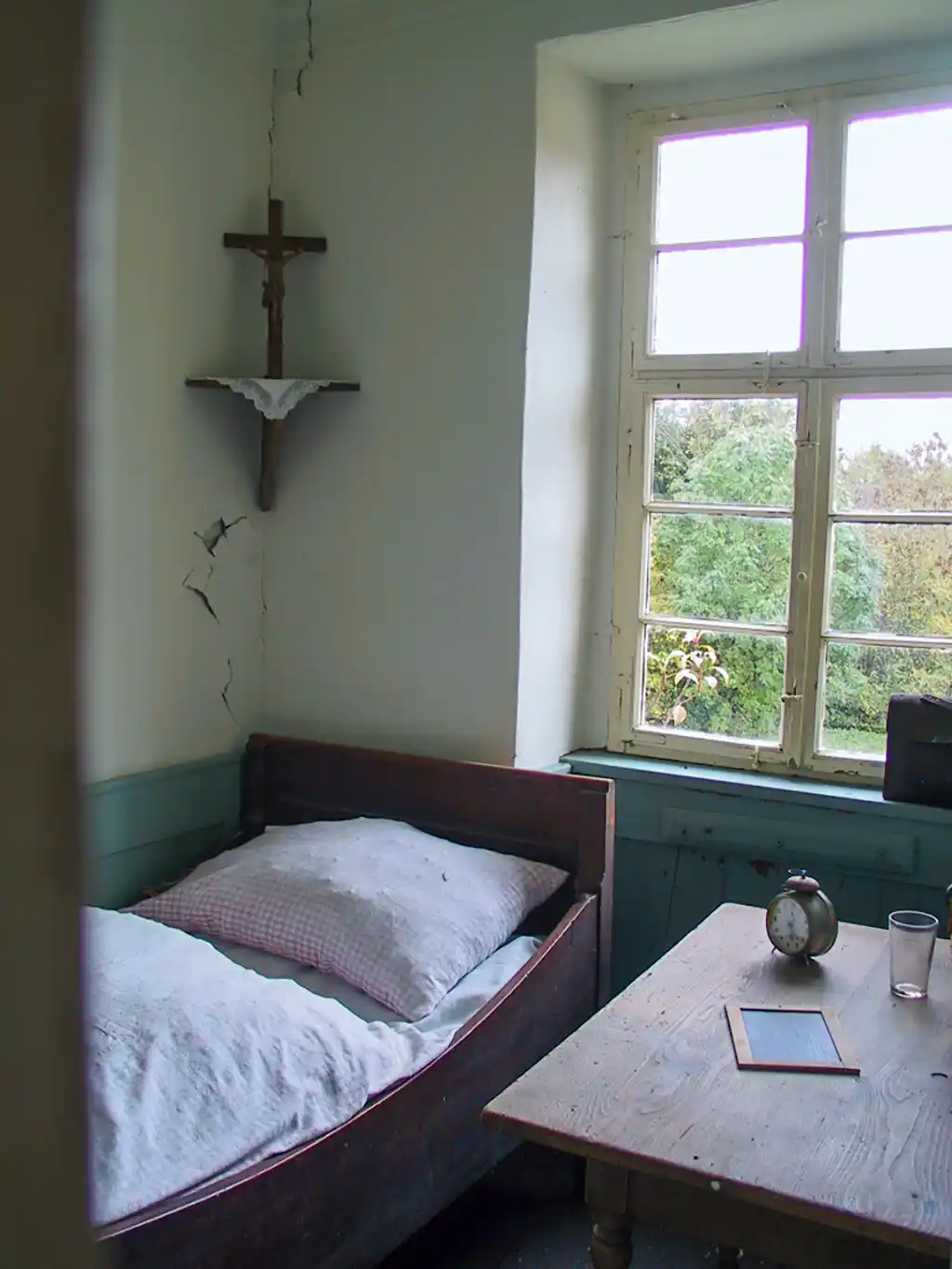 Schlafzimmer mit Holzbett, Nachttisch und Kruzifix an der Wand.