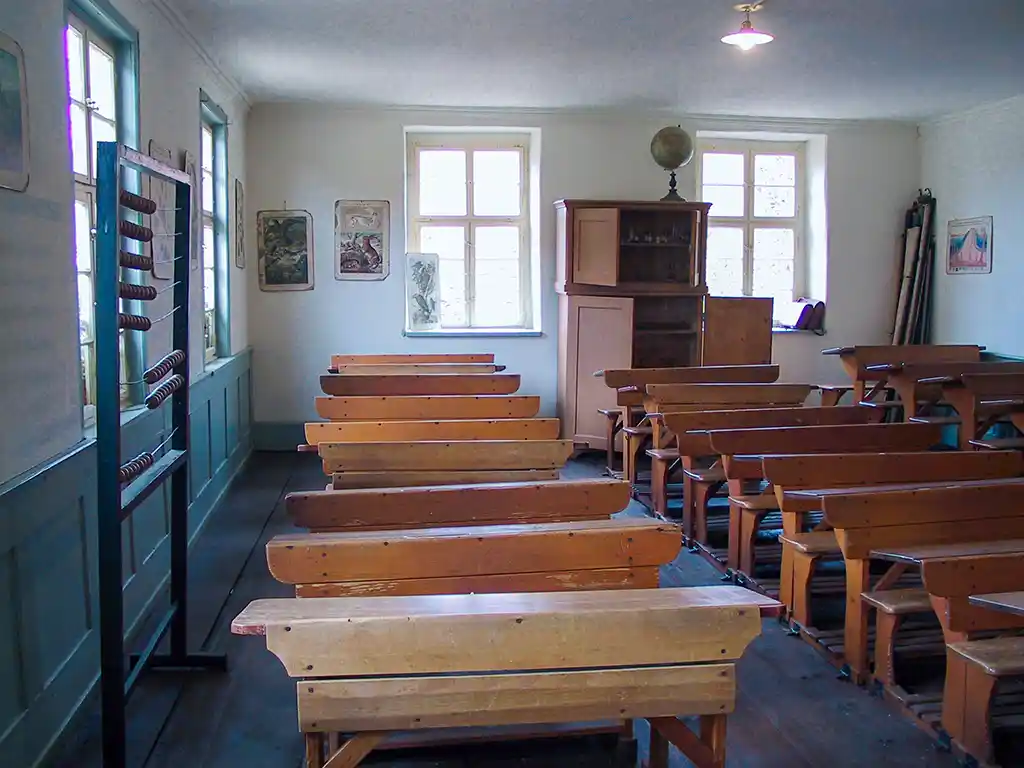 Ein traditionelles Klassenzimmer mit Holzschulbänken und einem großen Rechenschieber im Schul- und Rathausgebäude.