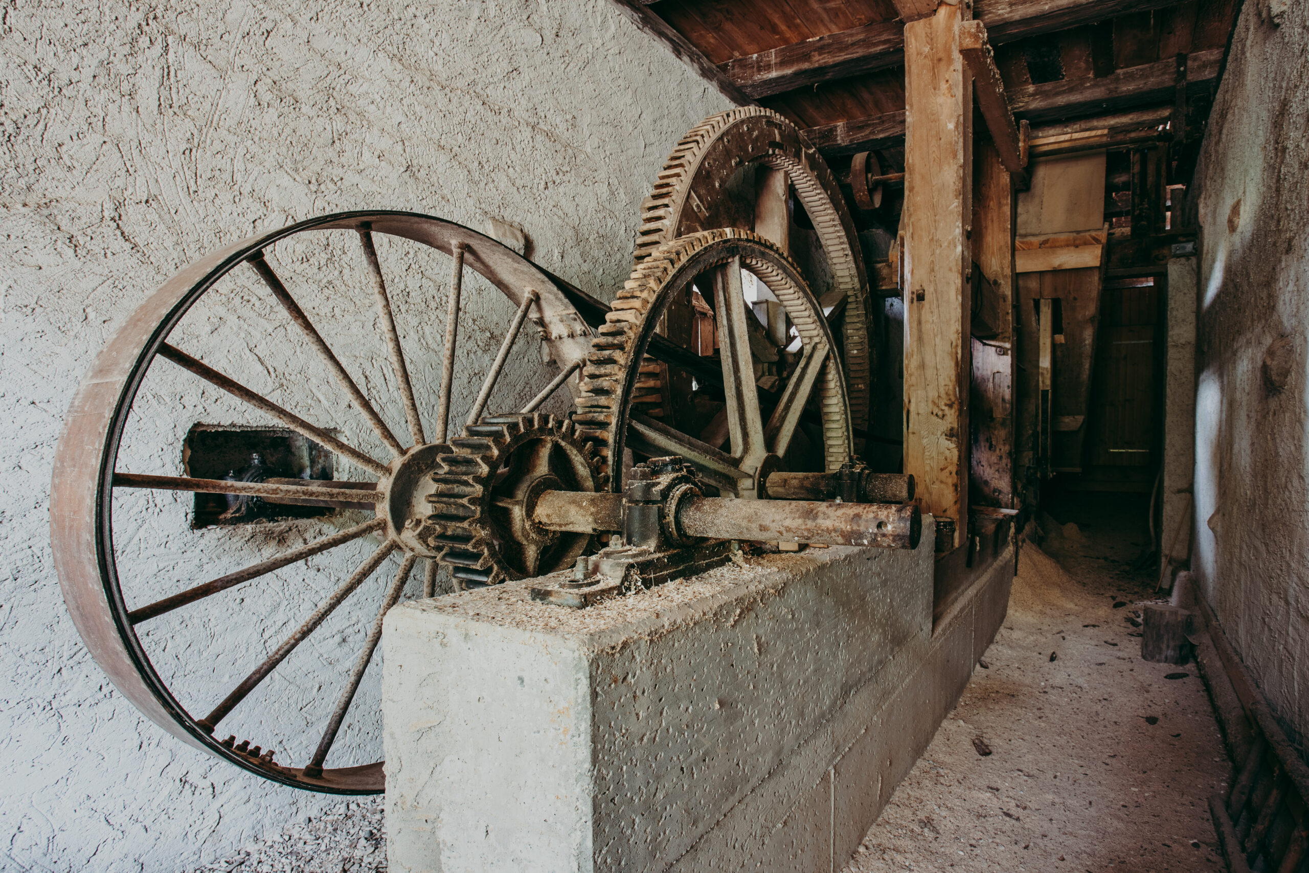 Foto: Mechanikraum im Sägewerk mit mehreren großen Zahnrädern aus Metall. Die Antriebseinheit ist auf einem Betonfundament montiert.