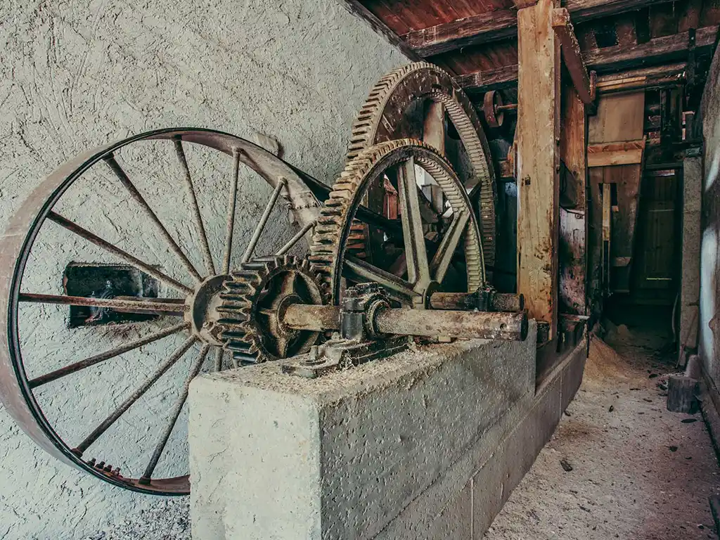 Foto: Mechanikraum im Sägewerk mit mehreren großen Zahnrädern aus Metall. Die Antriebseinheit ist auf einem Betonfundament montiert.