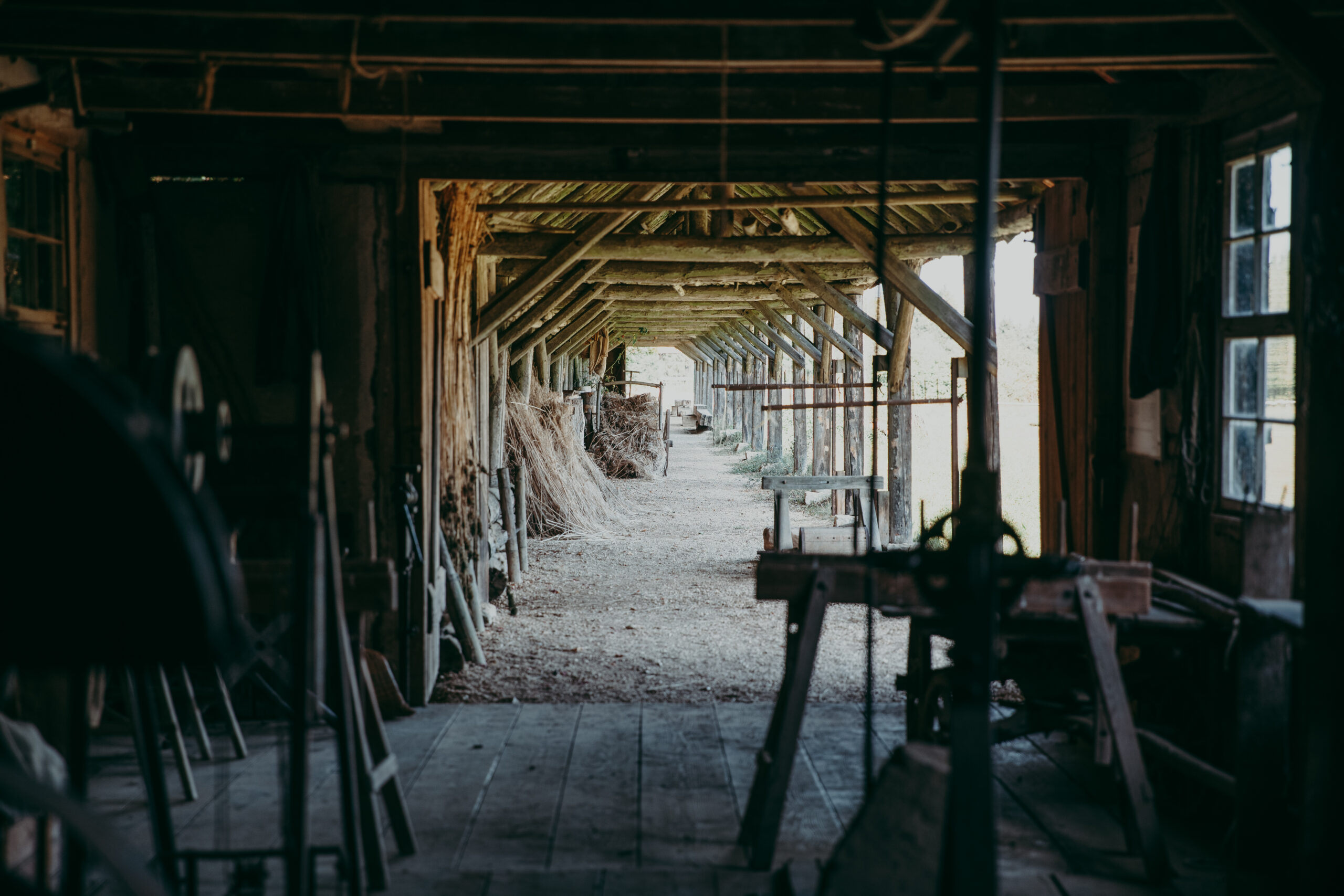 Foto: Blick vom Inneren der Seilerei durch den offenen Gang nach draußen. Links und rechts Maschinen und Werkzeuge, mittig ein langer Fluchtpunkt unter dem Dach entlang.